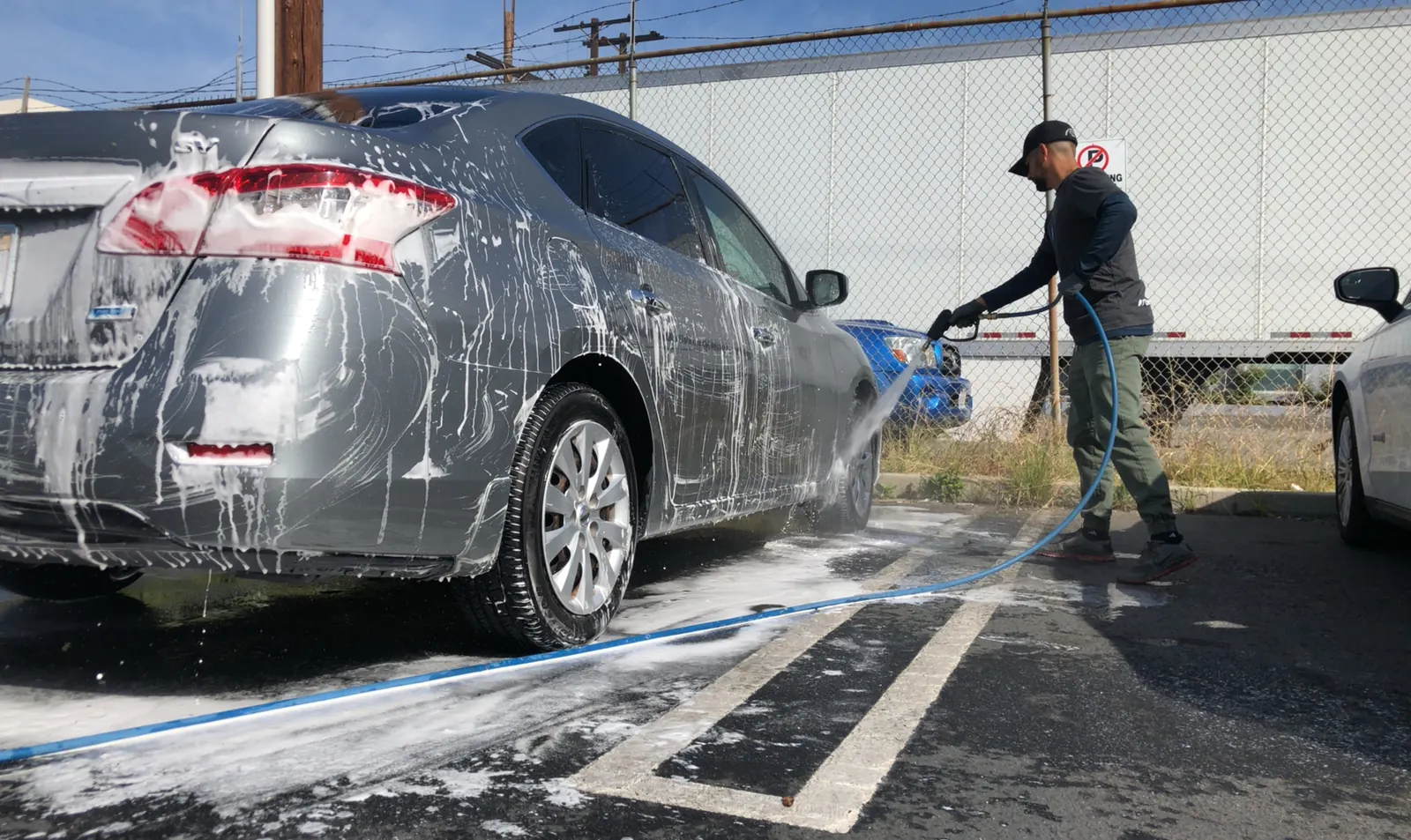 A professional foaming and washing a silver sedan